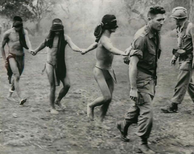 Soldier of the 1st Air Cavalry leads a group of blindfolded Montagnard men, suspected of working with the Viet Cong, 1966