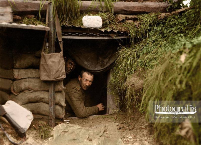 Two New Zealand soldiers look out of a dugout at the front line, Hébuterne, Pas-de-Calais on the 13th May 1918 The sign above the entrance reads; "The Diggers Rest. Board and residence. Cold showers when it is wet. Herr Fritz's Orchestra plays at frequent intervals." Hébuterne and its vicinity are of some significance in the history of New Zealand arms. Not only did the division finally arrest the German momentum there in March/April 1918, but it also became the start point of the Advance to Victory of August to November 1918. Hébuterne was the place where Sergeant (later Major) Reginald Stanley Judson of the Auckland Regiment won the Distinguished Conduct Medal, to which in the space of a month he would add a Military Medal and then the Victoria Cross at Bapaume. (text courtesy of christchurchcitylibraries.com) (Photosource - National Library of New Zealand - H577) Photographer Henry Armytage Saunders © Colourised by Tom Marshall at PhotograFix - Restored and Colourised Photos 2016.