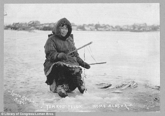 Inuk Woman poses over an ice fishing hole, several successful fish seen at her left-hand side