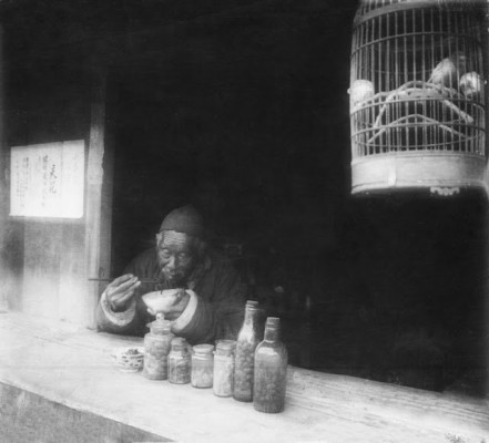 Old man eating noodles in his shop, bird in a cage, Shanghai, 1923