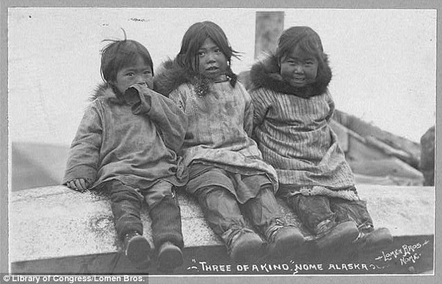 Three Eskimo children are seen seated side by side, their hoods removed to reveal smiles and playful eyes despite the cold climate otherwise adapted to by the locals