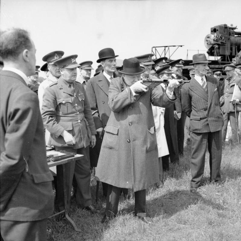 Winston Churchill tests a Sten Gun, 1941. Thompson is to the right of Churchill (in front of the crowd, in a pinstripe suit and tie)