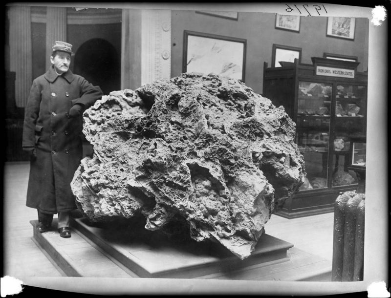 A security guard in uniform standing on a wooden platform with his arm resting on the specimen of Smithsonite from the Morning Star Mine, Oklahoma. 1906