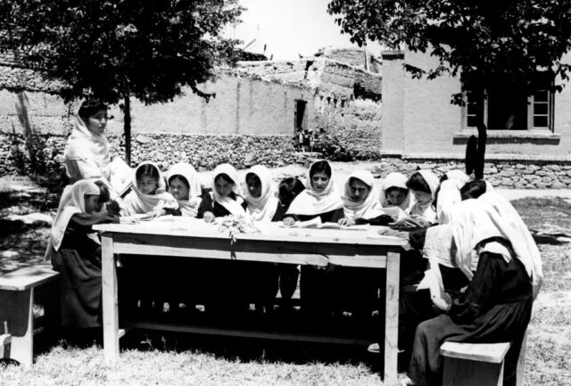 Students sitting at a desk outside with their teacher