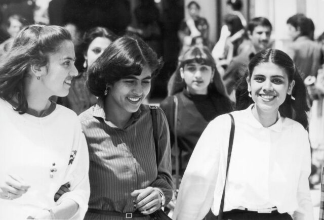 Three female students walking through a crowd