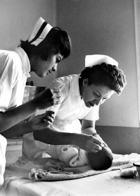 Two nurses standing over a baby that's lying on a table