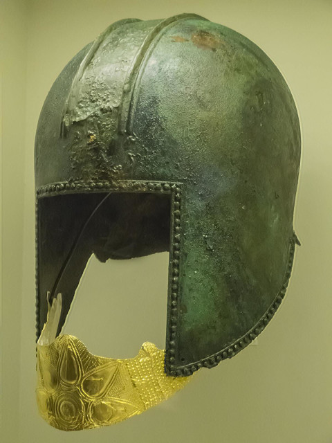 Funerary bronze helmet with gold mouth piece from the necropolis at Archontiko Greek 560-550 BCE. The gold mouthpiece is decorated with an embossed star. Embossed dots of various sizes in simple geometric forms cover the remaining surface.