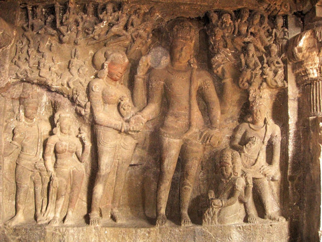 Wall carvings – A scene depicting the wedding of Shiva (four armed figure, right) and Parvati (two armed, left).source