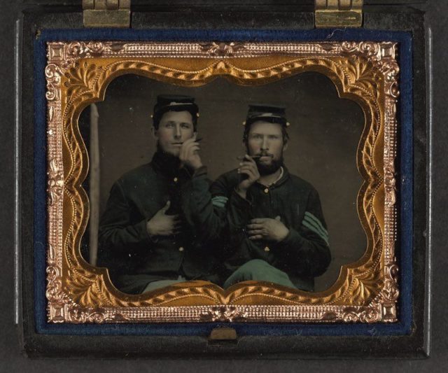 Unidentified soldiers in Union uniforms holding cigars in each others' mouths.