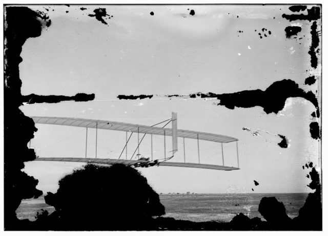 Left view of Wilbur gliding, Kitty Hawk Lifesaving Station and Weather Bureau buildings in distance Photo Credit 