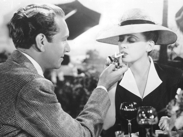 Paul Henreid lights Davis’ cigarette in Now, Voyager (1942), one of her most iconic roles. Photo Credit
