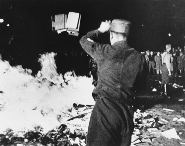 A member of the SA throws confiscated books into the bonfire during the public burning of "un-German" books on the Opernplatz in Berlin.