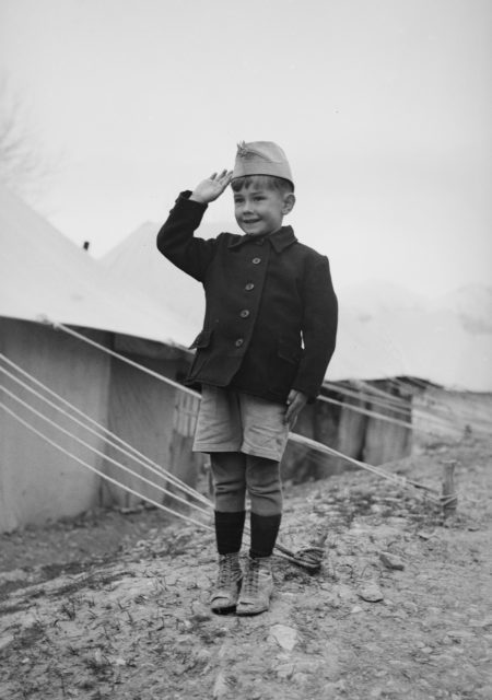 A-young-Polish-refugee-salutes-outside-his-tent. Photo Credit
