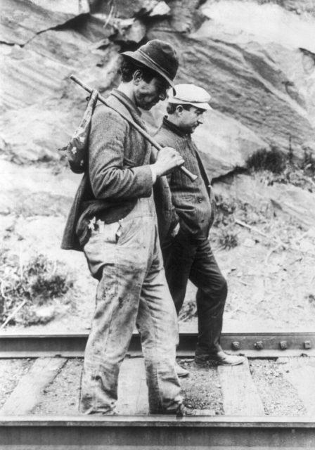 Two hobos walking along railroad tracks after being put off a train. One is carrying a bindle