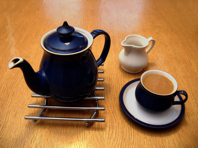 A ceramic teapot on a metal trivet, a cream jug, and a full teacup on a saucer.