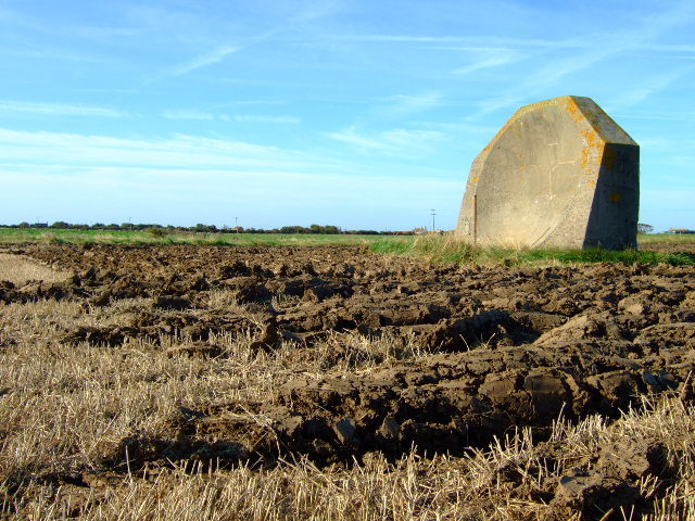 The farmland has been ploughed around the mirror. The rusty pole in front of the mirror had a microphone attached to it when listening for aircraft in the First World War. Author: John Poyser CC BY-SA 2.0