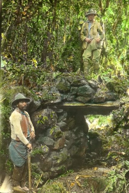 Bingham (upper right) with a local guide on a jungle bridge at Espiritu Pampa in Peru, hand-colored glass slide, 1911. Photo Credit