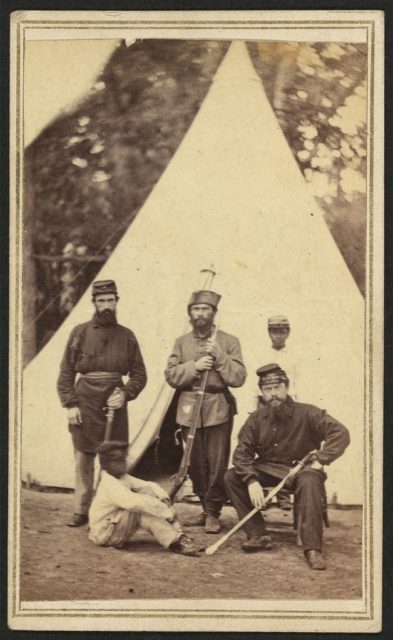 Three soldiers and two African American children, probably servants, posing in front of a tent. Photo Credit