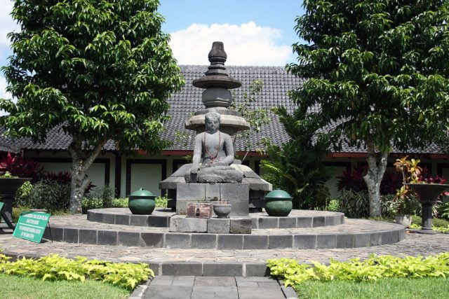 The Unfinished Buddha of the main stupa of Borobudur, transferred to the Karmawibhangga Museum. Behind it is a three-leveled parasol from Borobudur’s main stupa which was broken apart by a lightning strike. Photo Credit