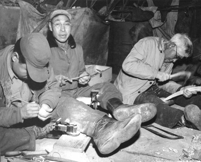 King Island locals making their ivory carvings and craftwork beneath their skin umiaks on the beach near Nome where they have a summer camp. Only the simplest of hand tools are used for carving the walrus ivory tusks.