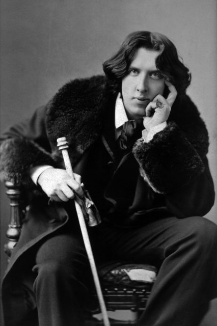 Portrait of Oscar Wilde sitting down holding a cane.