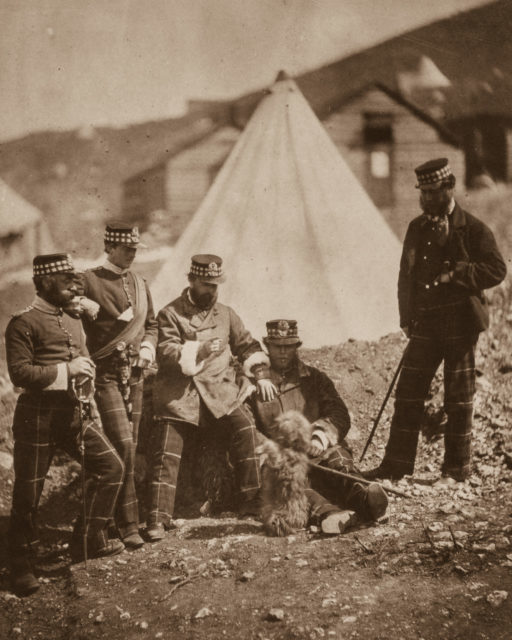 Officers of the 71st Highlanders pose with a dog in a British encampment.