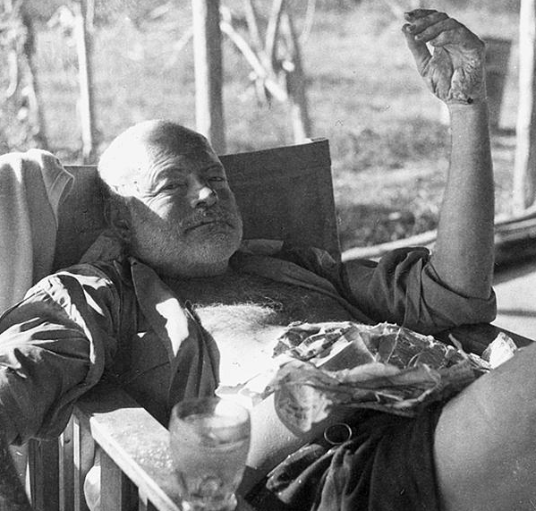 Hemingway at a fishing camp in 1954. His hand and arms are burned from a recent bushfire; his hair was burned in the recent plane crashes