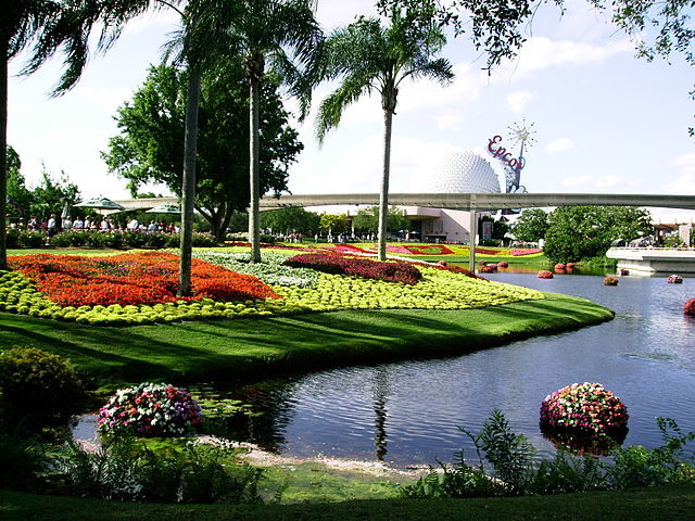 This image shows the landscape of Epcot which includes landscaped gardens, lakes, and trees, as well as the famous Spaceship Earth and the Walt Disney World monorail.