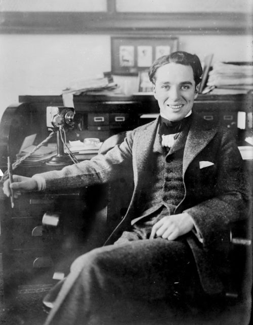 Charlie Chaplin seated at desk.