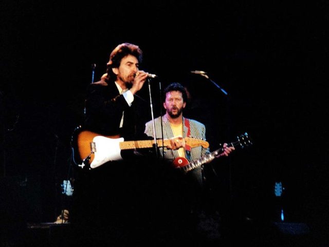George Harrison and Clapton at the Prince’s Trust Concert, Wembley Arena, 1987. Photo by Steve Mathieson. CC BY-SA 2.0