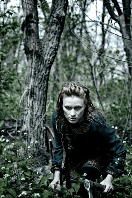 Scandinavian woman posing with sword and axe in a forest