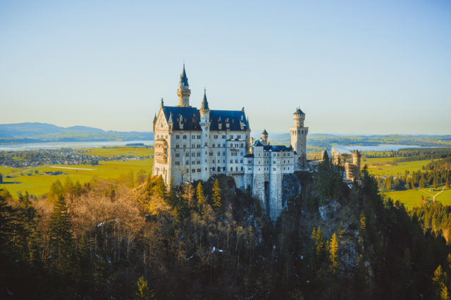 Neuschwanstein Castle on top of hill against beautiful natural landscape on sunny spring day. New Swanstone Castle is a 19th century Romanesque Revival palace on a rugged hill above the village of Hohenschwangau near Füssen in southwest Bavaria, Deutschland.