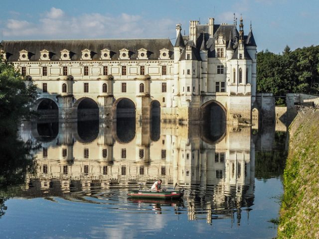 A fisherman in a boat creates ripples in the reflection of Chenonceaux Castle in the Loire Valley, France.