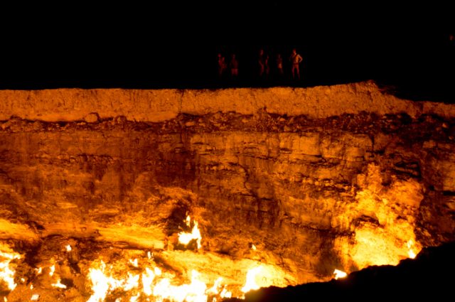 The Darvaza Gas Crater in Turkmenistan at sunrise. Gas coming from the ground is burning in the crater. The diameter of the hole is about 70 m. People can be seen at the edge of the crater illuminated by the light from the fire.