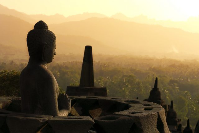 One of the many Buddha statues sitting inside a stupa on the top terraces of the temple facing a setting sun