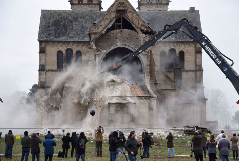 Spectators and journalists look on as the desacralized St Lambertus church in Erkelenz-Immerath, western Germany, is being demolished on January 8, 2018, in order to make possible brown coal surface mining. (Photo credit:HENNING KAISER/AFP/Getty Images)