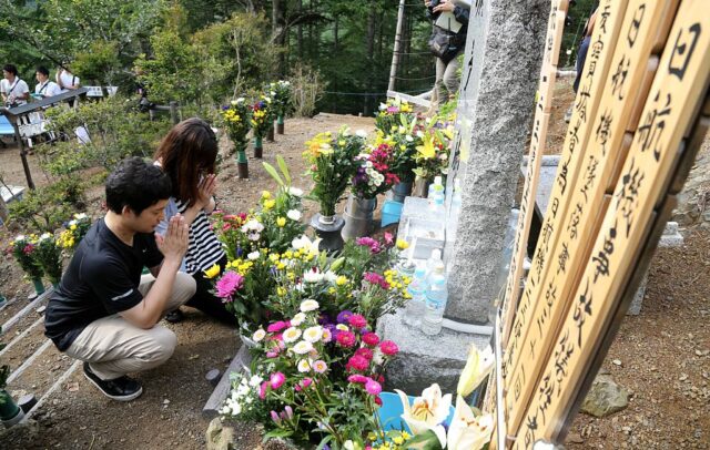 Two individuals praying at a memorial dedicated to the victims of Japan Air Lines Flight 123