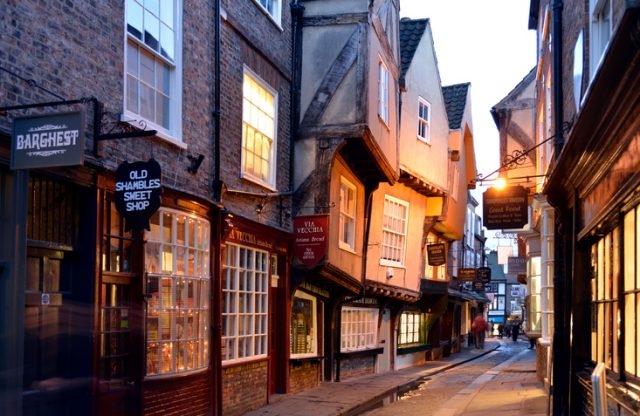 Shambles is probably the most famous street in York. Shambles has been a Shopping street since Tudor times and remains almost unchanged to this day and attracts tourists in the thousands.There are people in the scene but none of them are recognisable due to a slow shutter speed. Although the sky is white it was almost the last light of the day. The street was very dark and the lights were coming on.