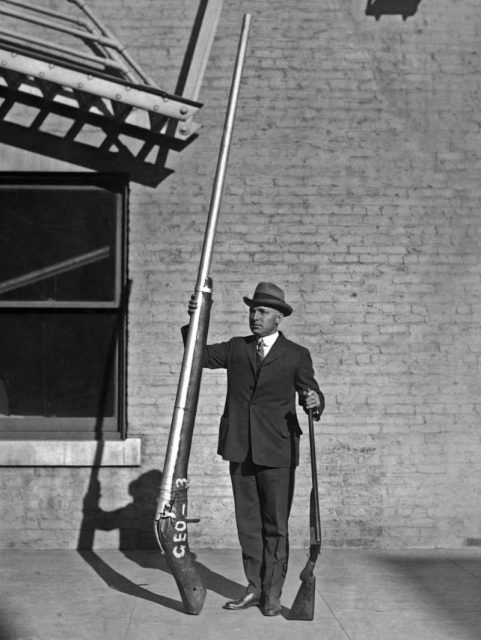 Chief United States Game Warden George A. Lawyer, with an illegal 10’9″ shotgun weighing 250 pounds, which was used for duck hunting. 1920.