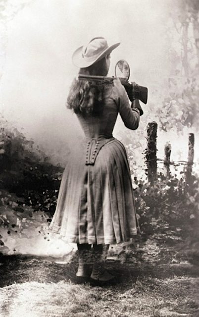 Annie Oakley shooting over her shoulder using a hand mirror.