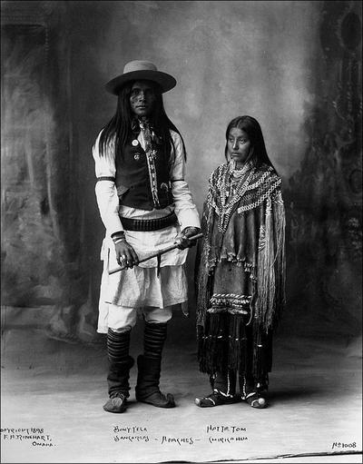 A studio photograph depicting a young Apache couple, both wearing traditional leather moccasins.
