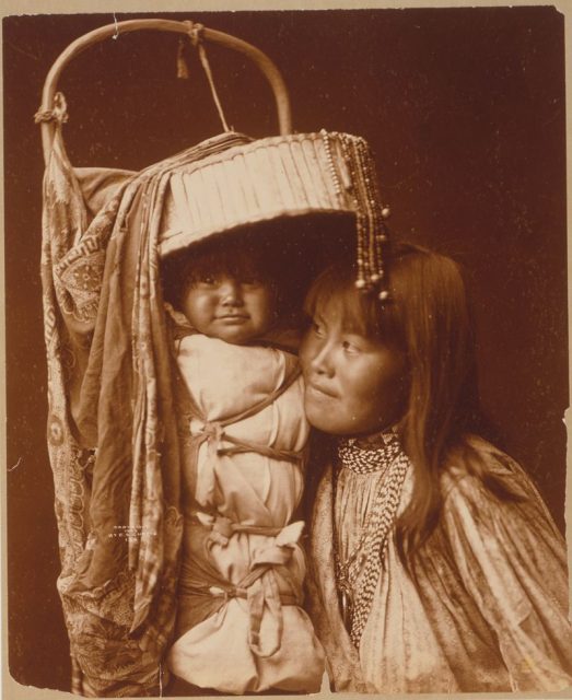 Woman with a baby tightly swaddled in the beautifully crafted cradleboard.