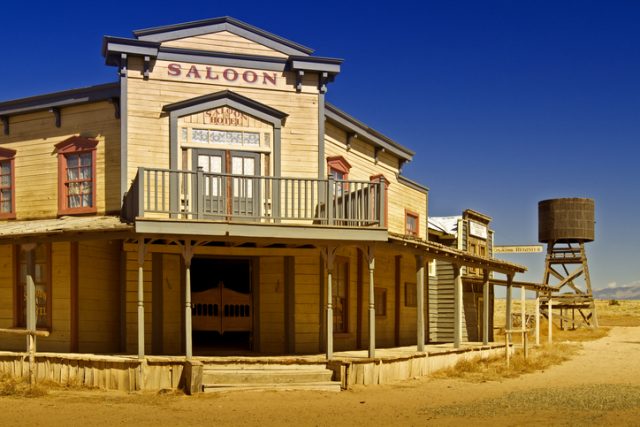 A saloon, telegraph office, and wooden water tower along the dirt road of an old American western town