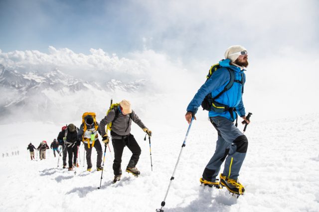 A group of mountaineers approach the summit of a snow capped mountain.