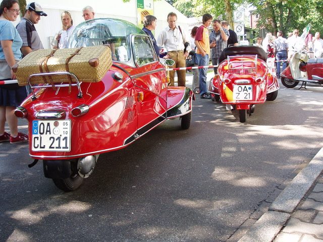 Two red Kabinenrollers, one with a case fixed to the luggage rack, being admired by enthusiasts