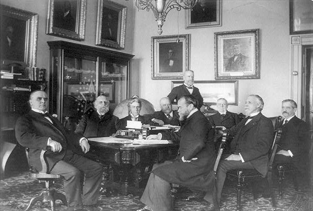 President McKinley and his cabinet, 1898. At far left: William McKinley. Left to right in back of table: Lyman J. Gage, John W. Griggs, John D. Long, James Wilson standing, and Cornelius N. Bliss. Left to right in front of table: John Hay, Russell A. Alger, and Charles E. Smith