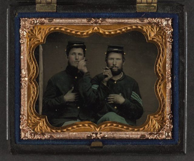 Unidentified soldiers in Union uniforms holding cigars in each others’ mouths.