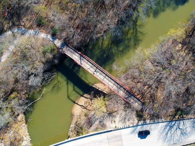 A drone shot from above Old Alton Bridge – Goatman’s Bridge – showing the span over the waterway and a single man laying on the bridge for reference. Photo by Pixelsyndicate CC BY-SA 4.0