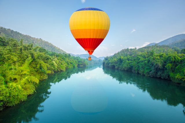 Hot air balloons flying over a river.
