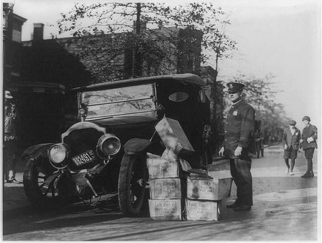 Policeman guards a wrecked car and cases of moonshine.